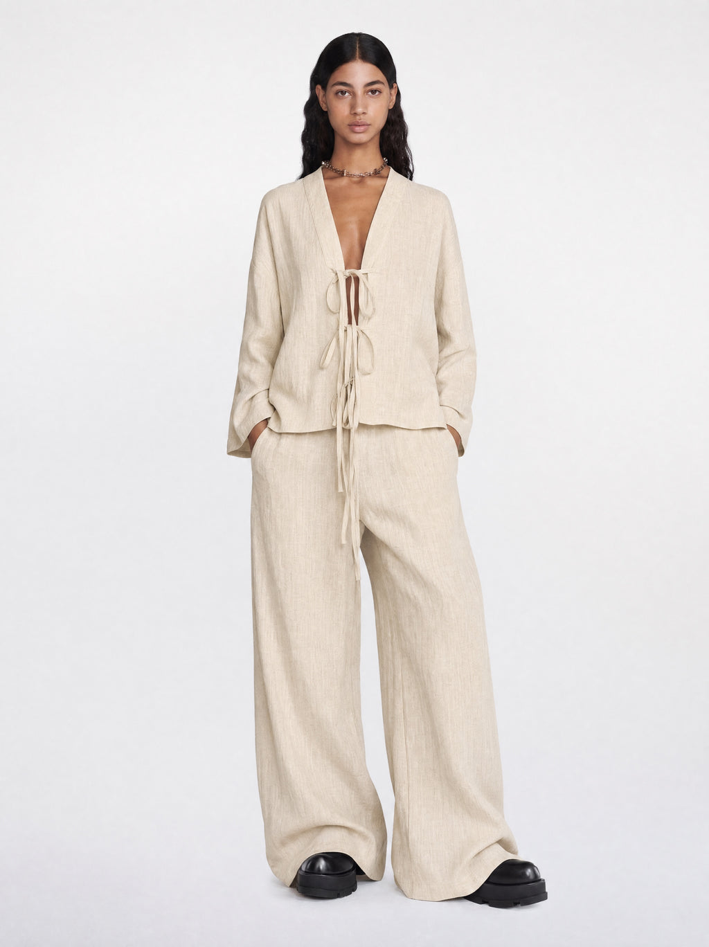 Woman wearing a beige outfit with wide-leg pants and a matching top on a white background