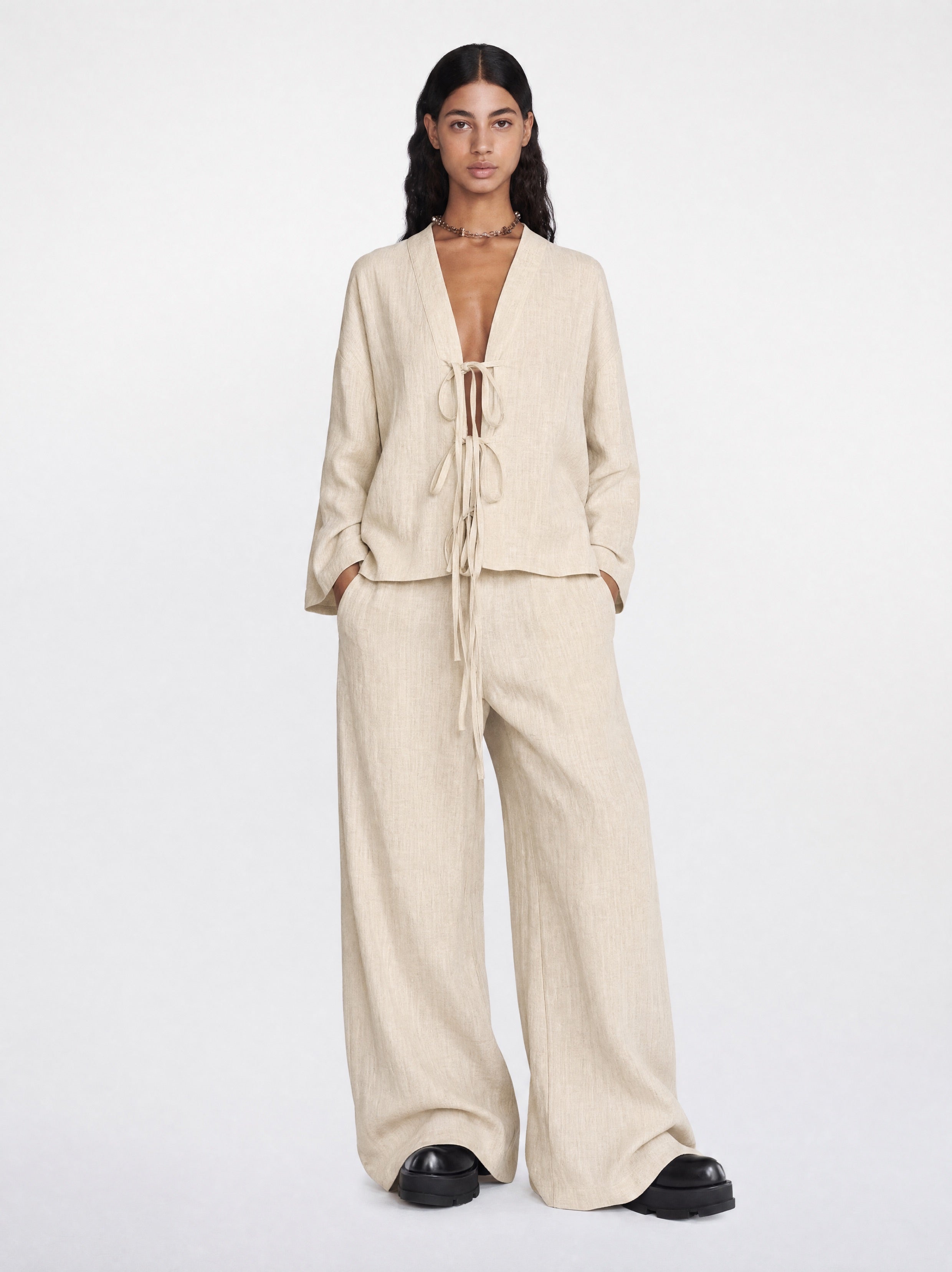 Woman wearing a beige outfit with wide-leg pants and a matching top on a white background